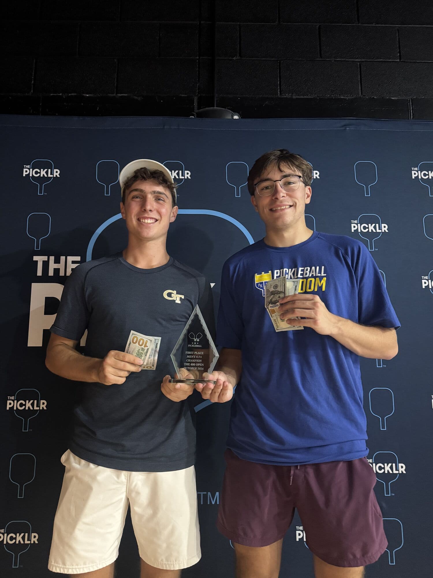 Two champions holding their trophy and cash prize