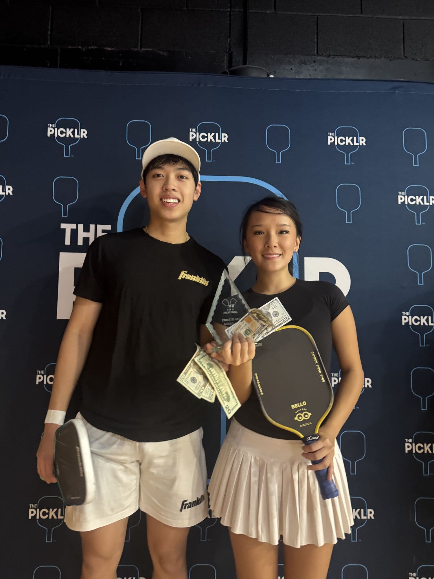 A mixed doubles team holding their trophy and cash prize